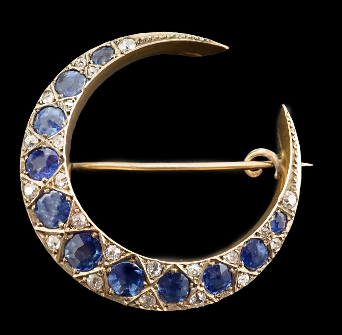 An early 20th century gold, graduated sapphire and diamond cluster set crescent brooch
